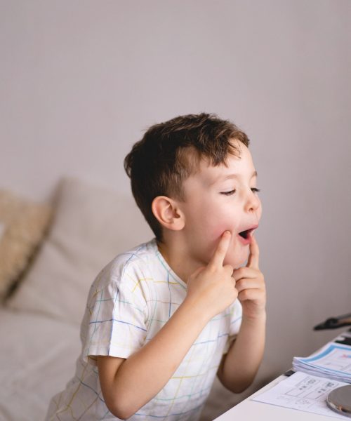 Speech therapy concept. Cute little boy pronouncing sound O looking at mirror doing an online Speech therapy lesson through a laptop